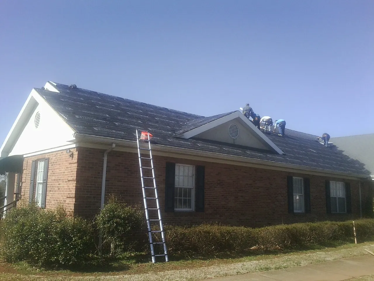 Crew tearing shingles off a brick ranch roof with a ladder set — Metal Roof Repair work by our crew in Hemet