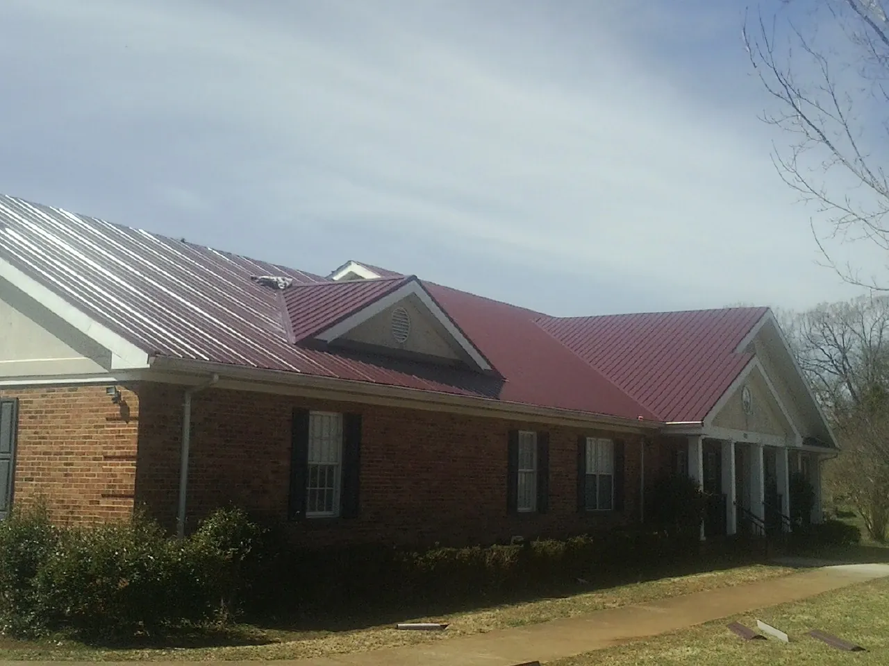 Red metal roof with gabled entries on a long brick building, from a Hail Damage Roof Repair job in Hemet