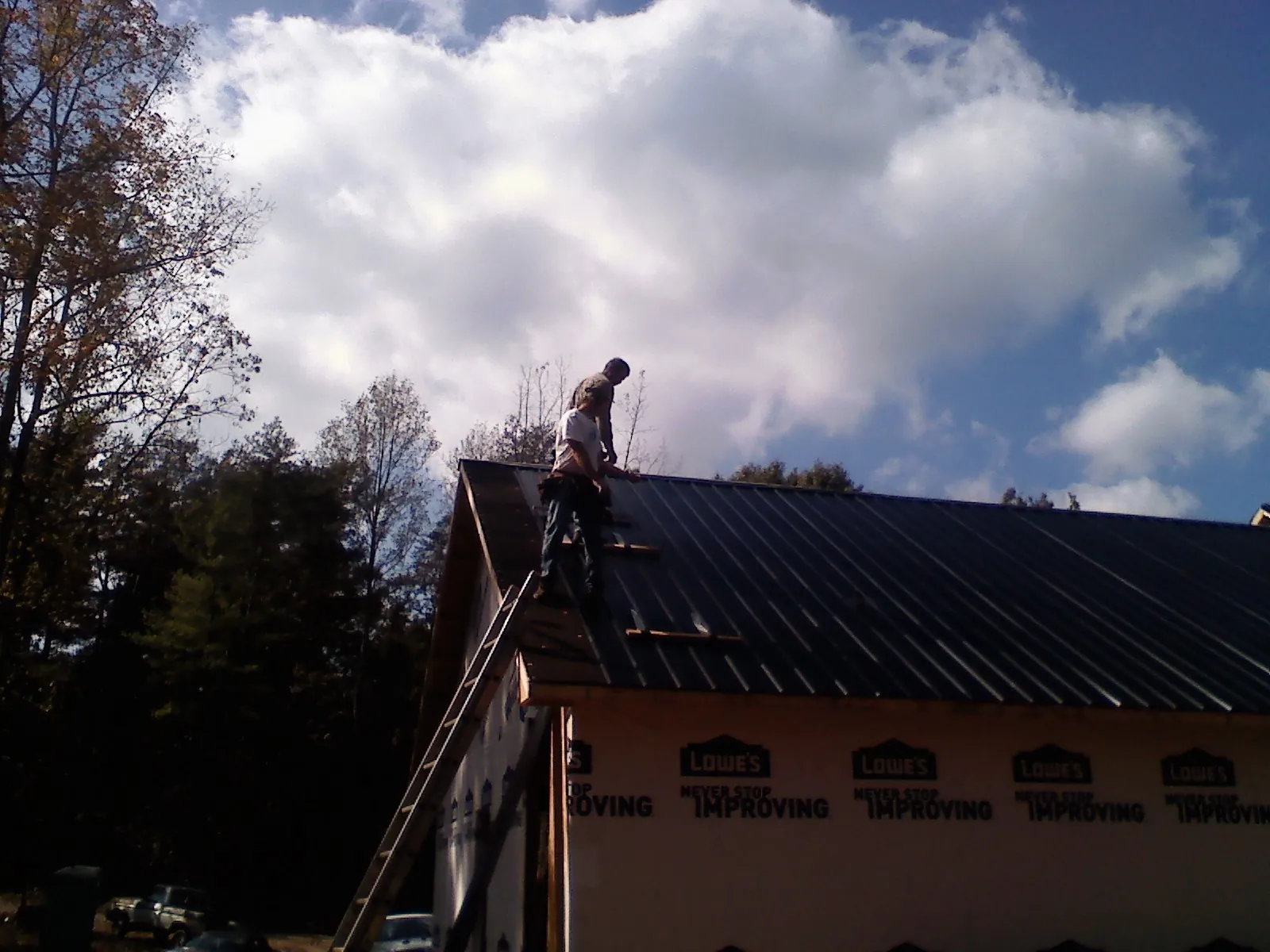 Roofer fastening dark metal panels high against a cloudy sky, from a Roof Inspection job in Hemet